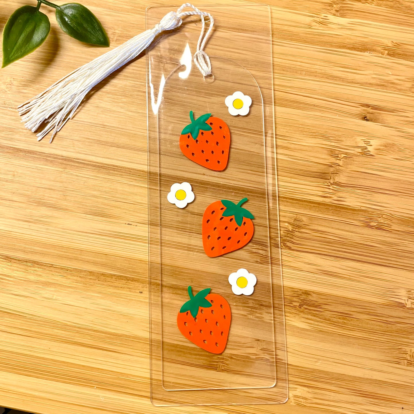 Clear acrylic bookmark with strawberry designs on a wooden surface