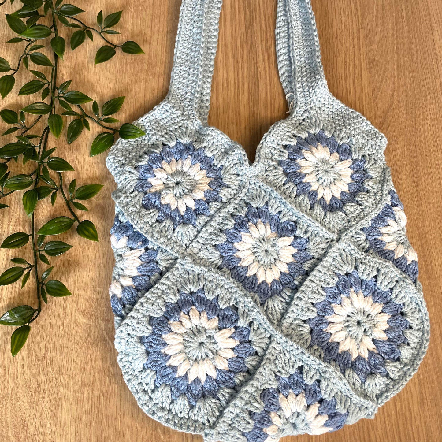 Crocheted bag with floral patterns on a wooden surface with green leaves.