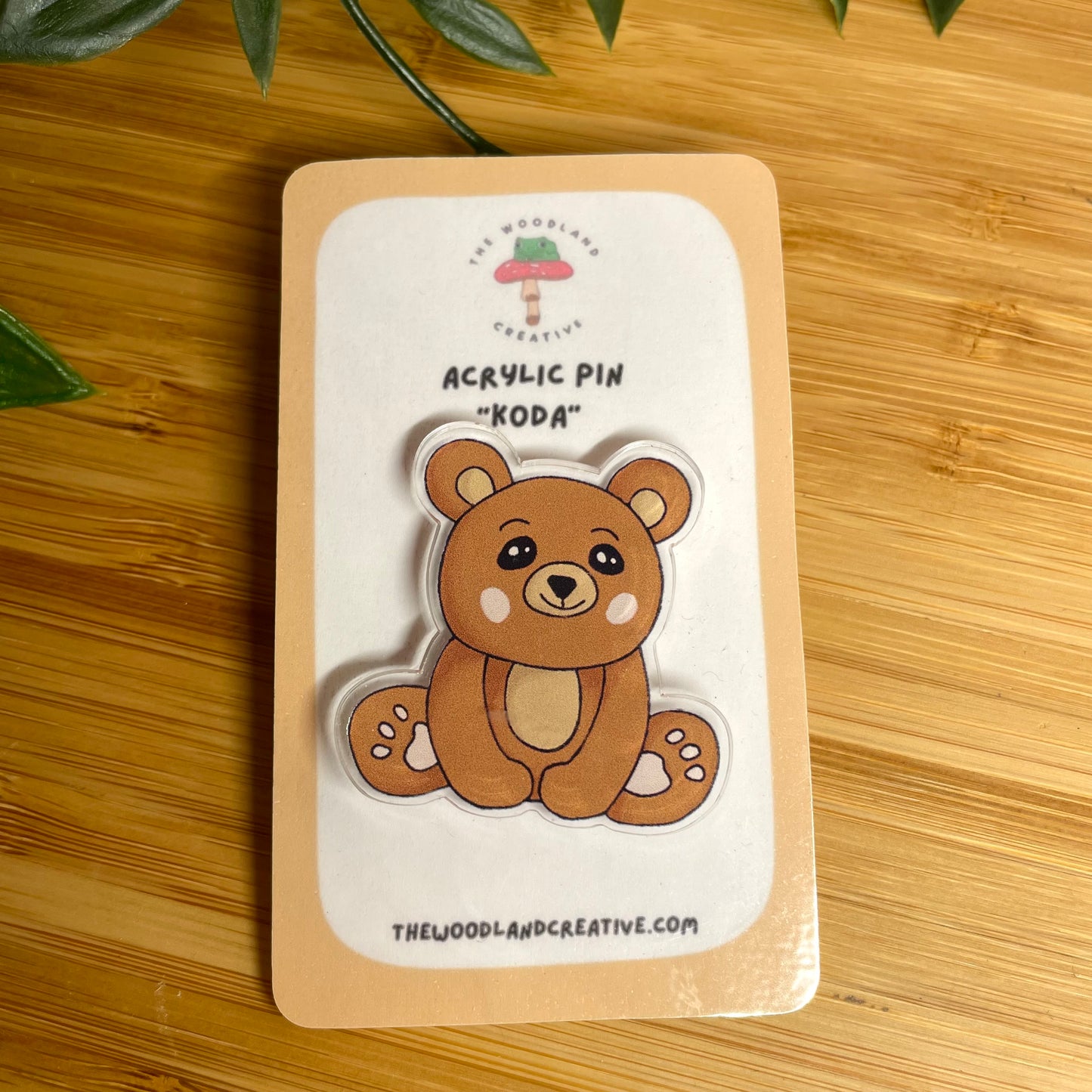 Acrylic pin of a bear on a cardboard backing with branding information, placed on a wooden surface.