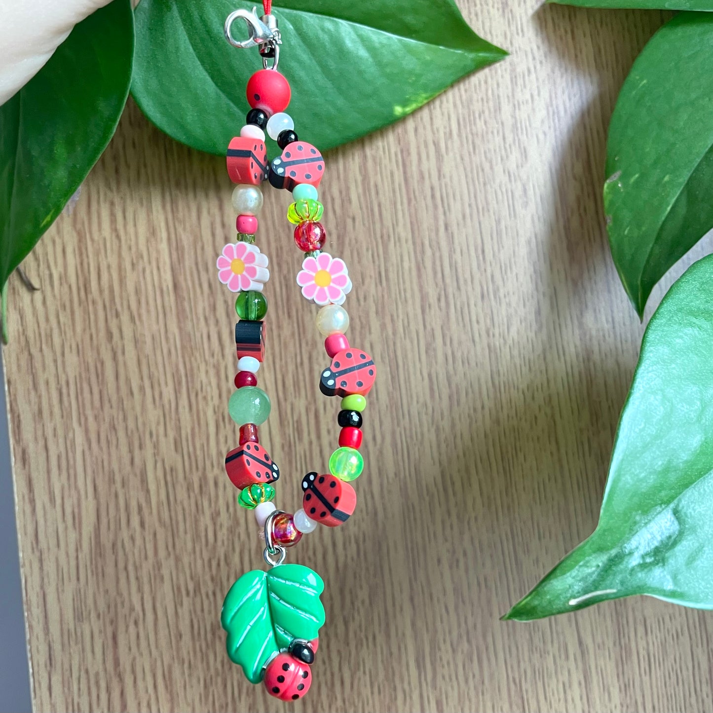 Colorful beaded keychain with ladybug and flower designs on a wooden surface with green leaves.