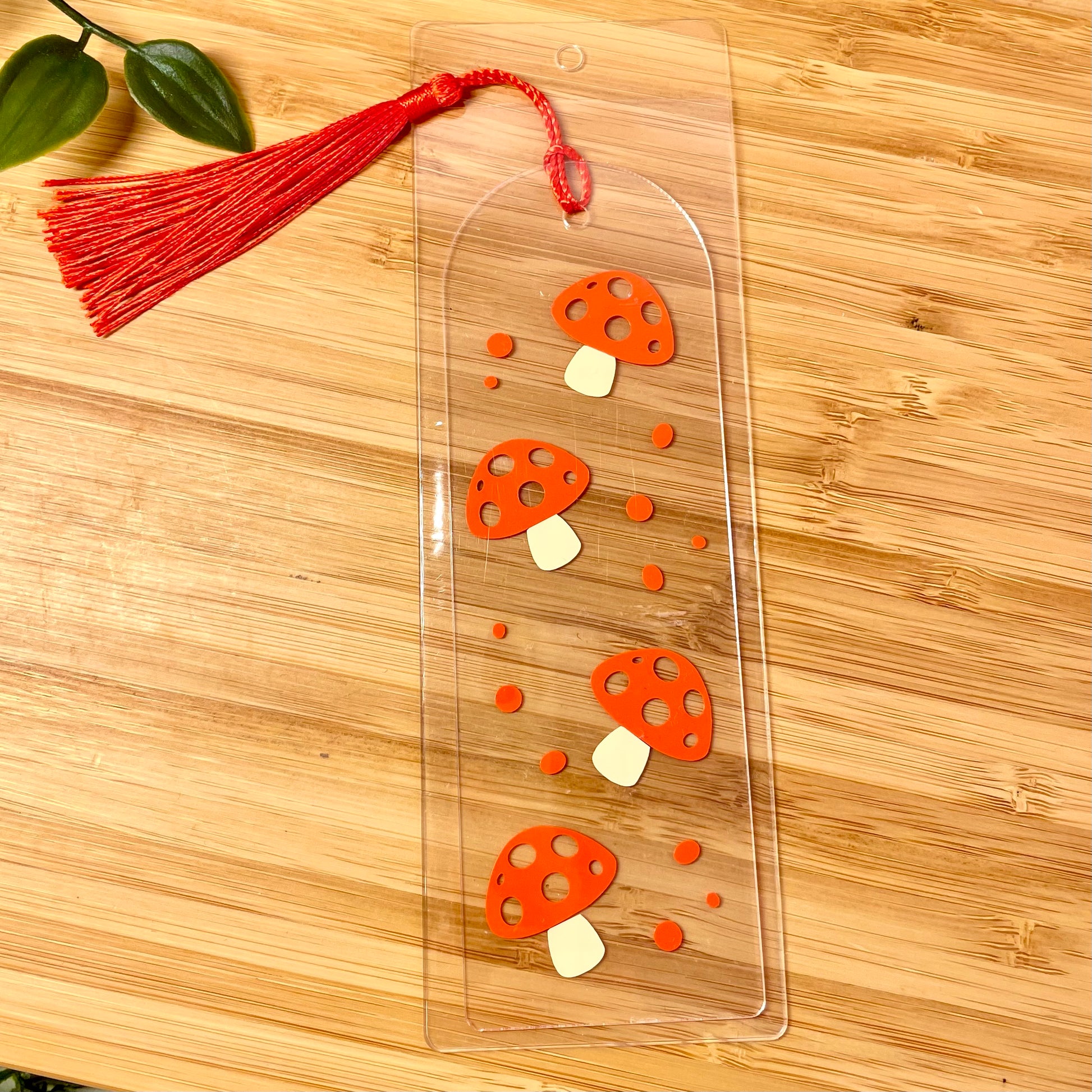 Clear bookmark with red tassel and red mushroom design on a wooden surface
