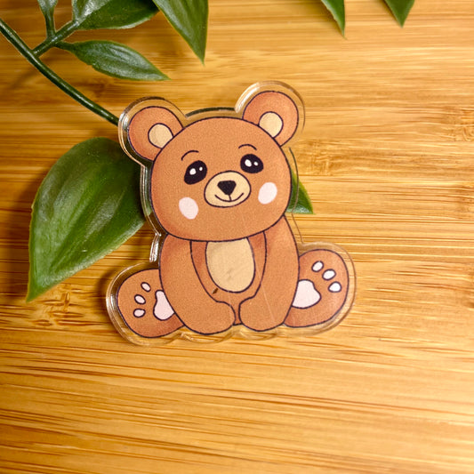 Bear-shaped keychain on a wooden surface with leaves in the background